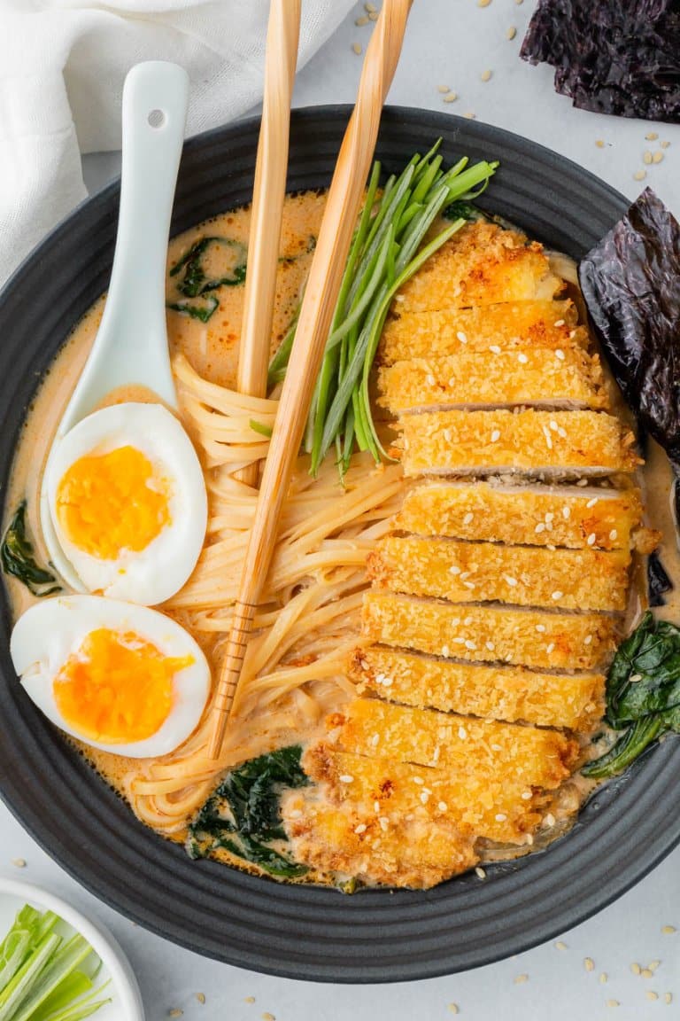 chicken katsu ramen in a black bowl with chopsticks and a soft boiled egg on top