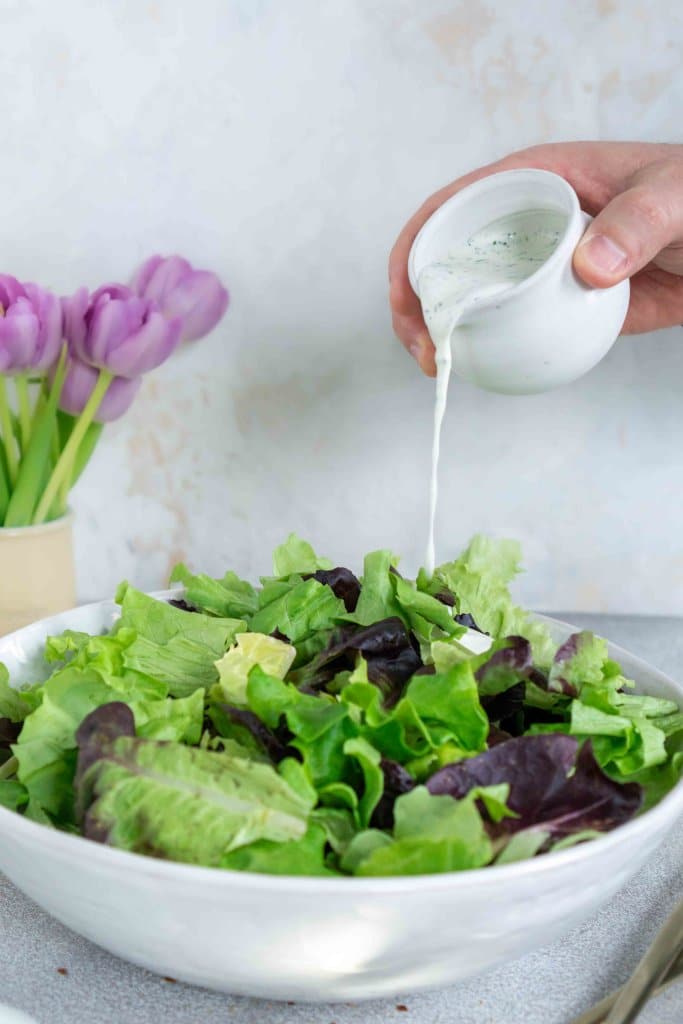 pouring herb ranch dressing on a salad