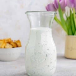 herb ranch dressing in a glass jar with croutons and flowers in the background