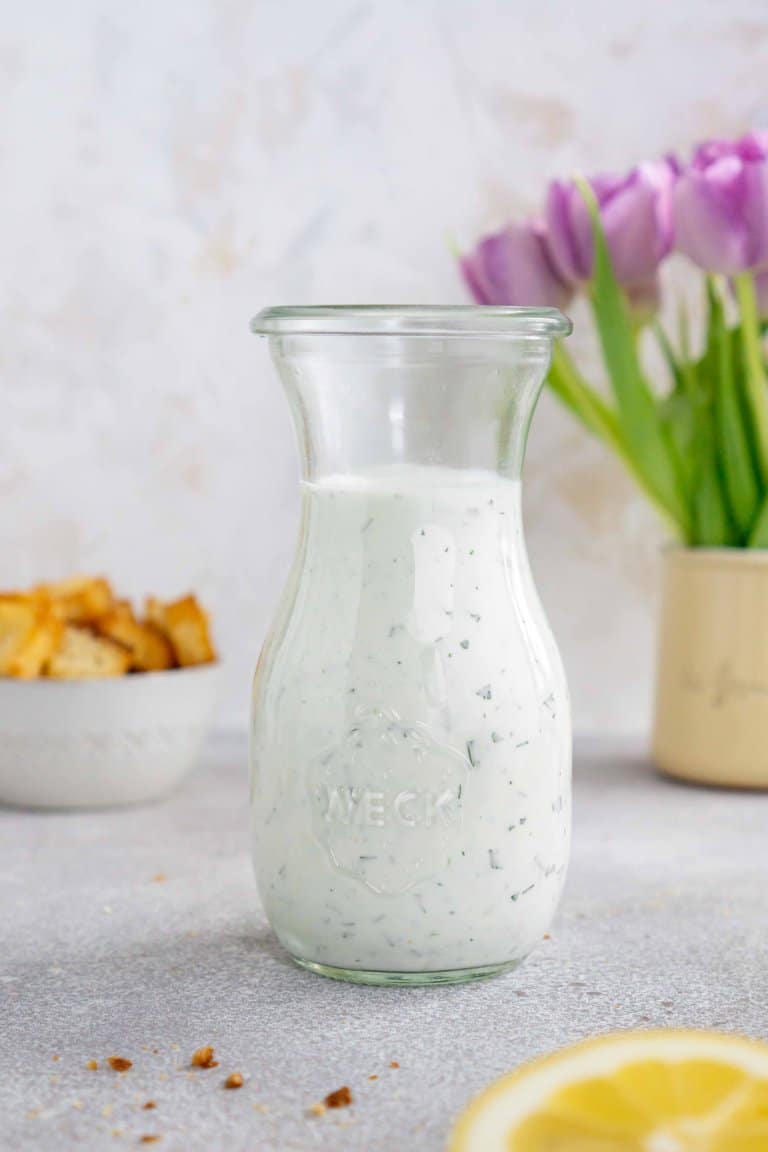 herb ranch dressing in a glass jar with croutons and flowers in the background