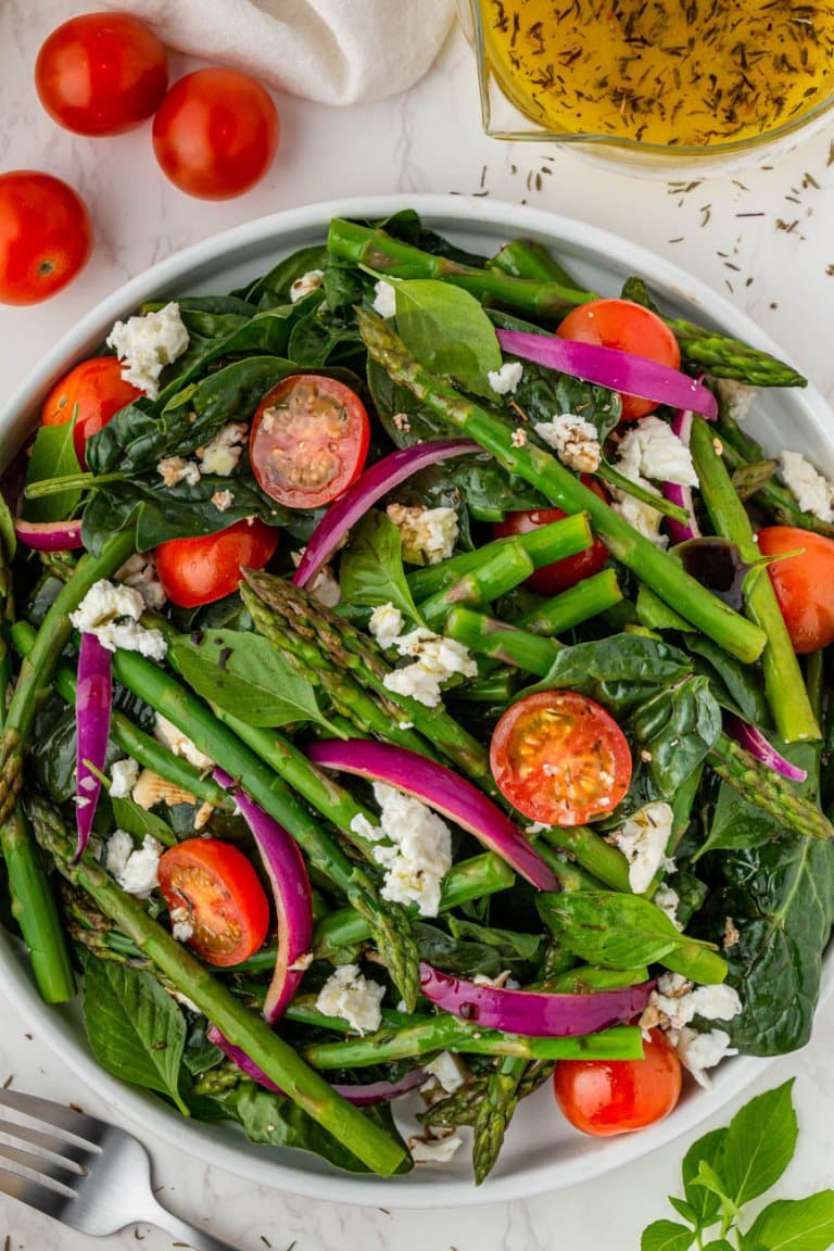 asparagus salad with feta, tomatoes, and red onions in a serving bowl with lemon vinaigrette to the side