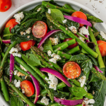 asparagus salad with feta in a serving bowl with tomatoes and red onions