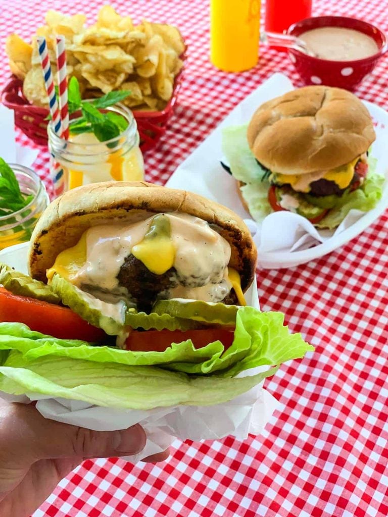 close up of burger with tomato and lettuce with red checkered table cloth in background Labor Day food ideas