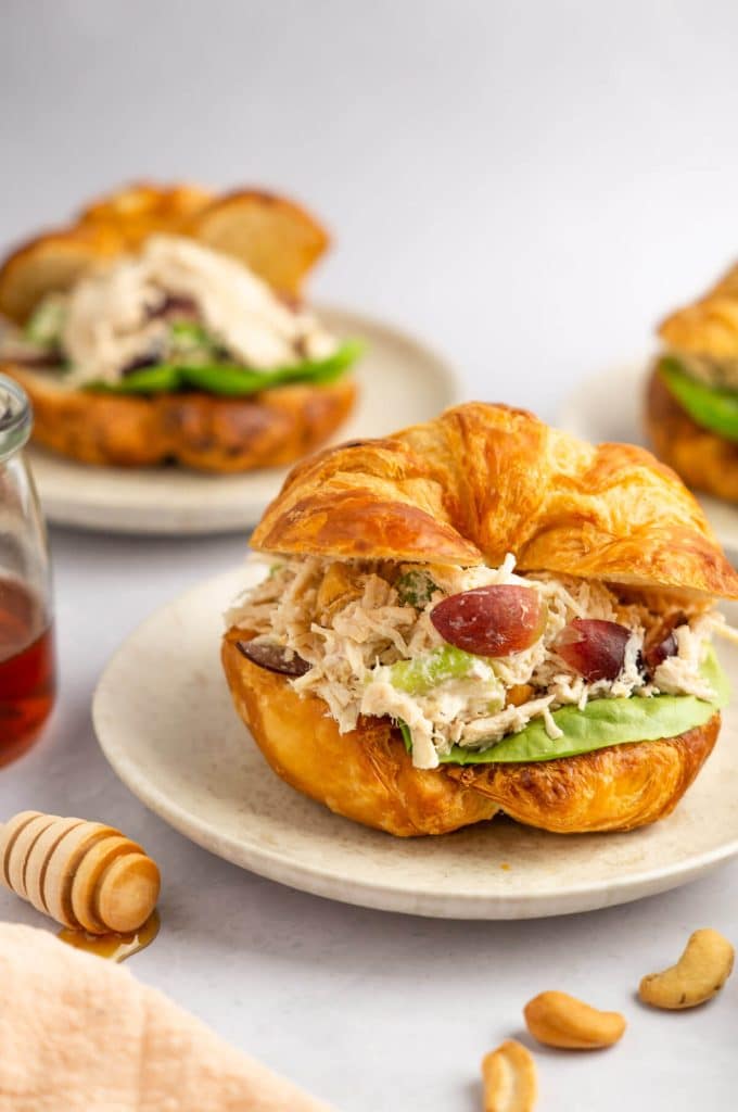 chicken salad on a croissant with grapes on plate with more sandwiches in background