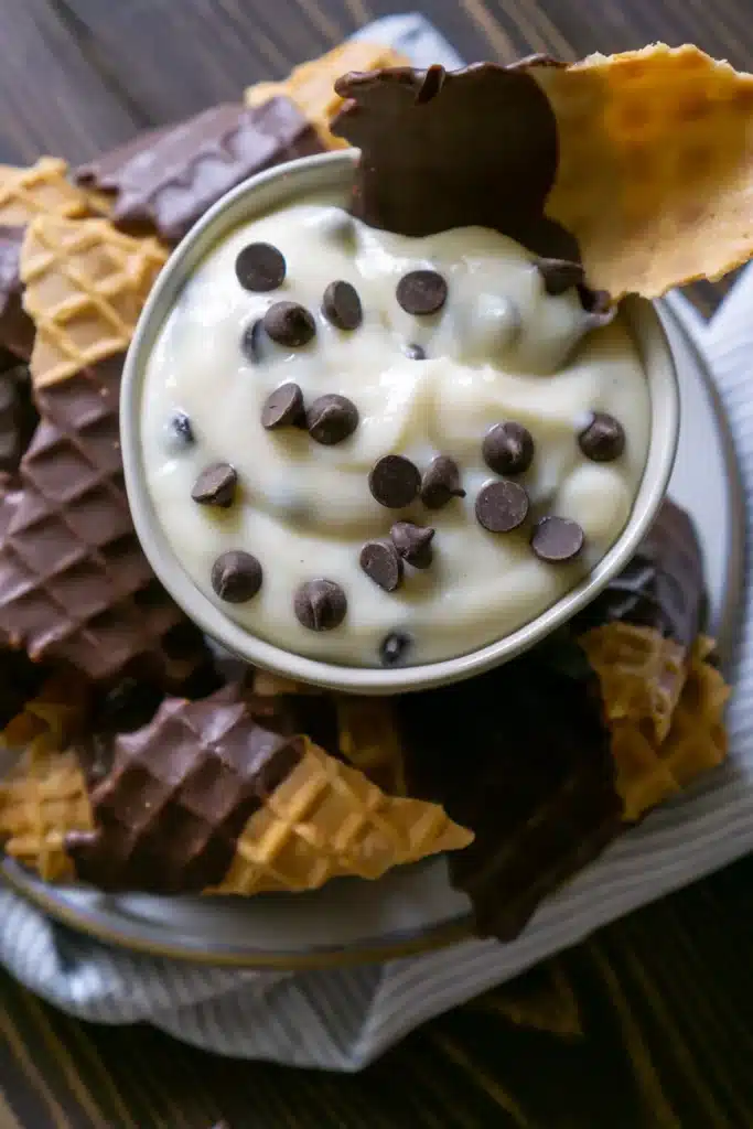 overhead view of cup of cannoli dip with chocolate chips surrounded by chocolate dipped waffle cone pieces