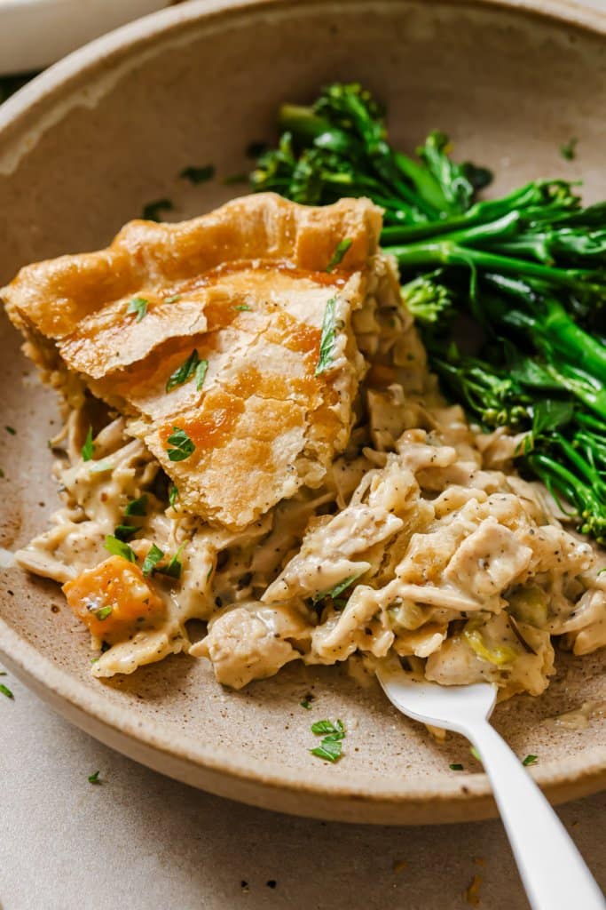 a piece of turkey pot pie on a plate with broccolini and a fork