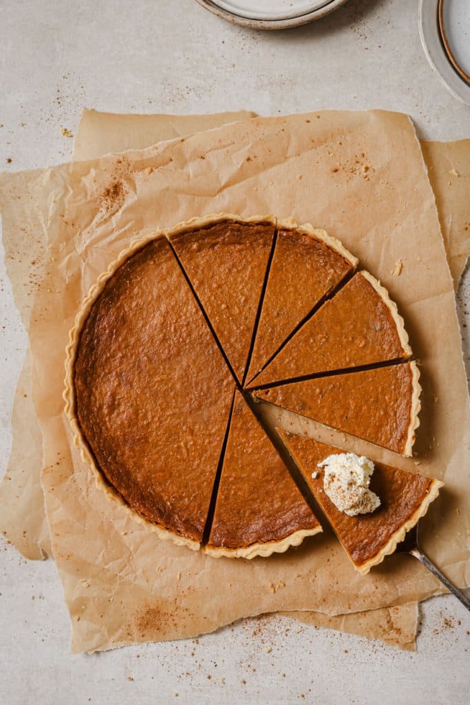 sweet potato pie cut into slices on brown parchment paper and whipped cream on one slice