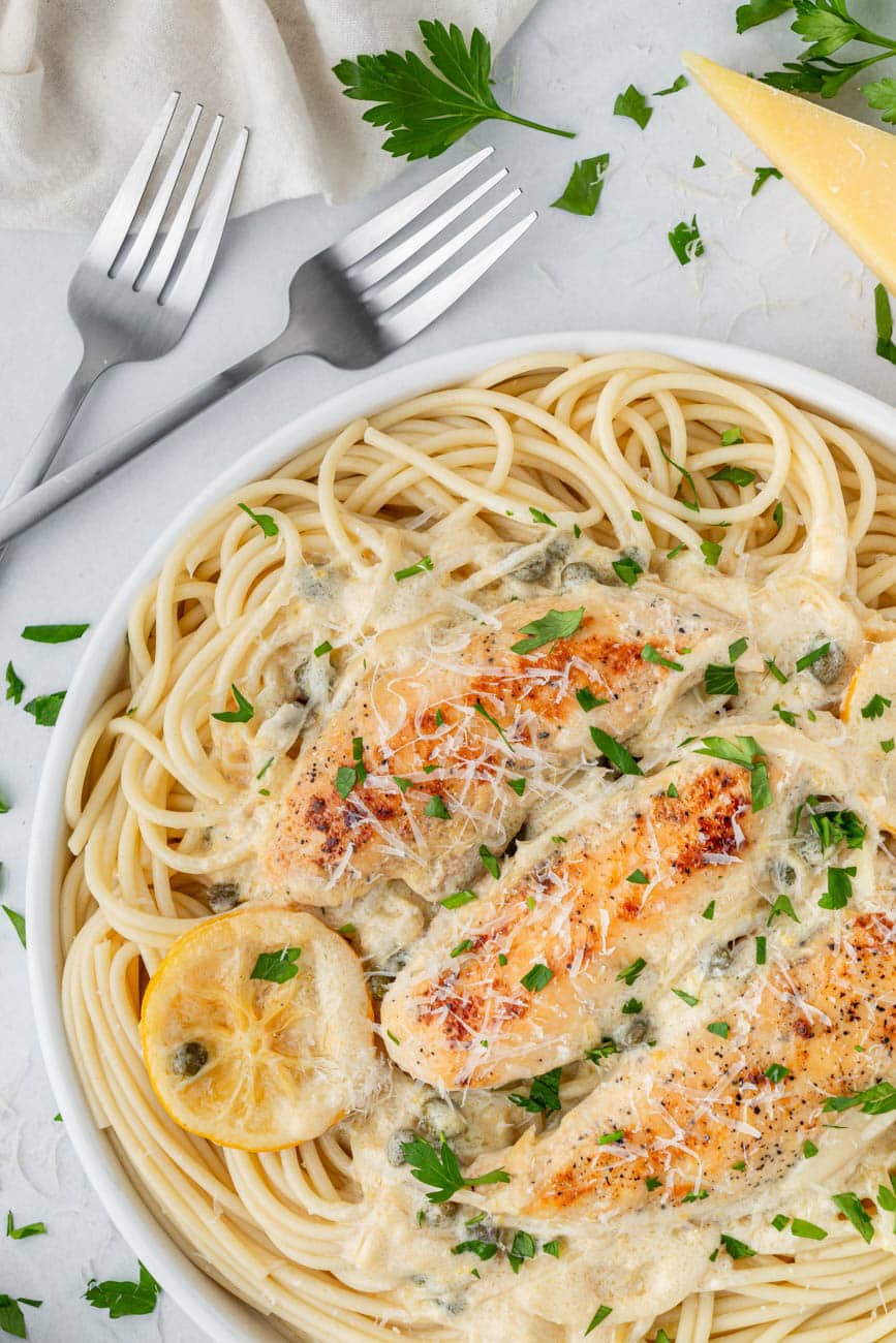 Chicken piccata sauce on chicken over a bowl of pasta with two forks on the side.