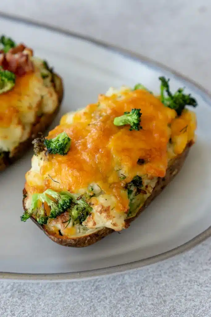 close up of twice baked potato with cheese and broccoli on white plate