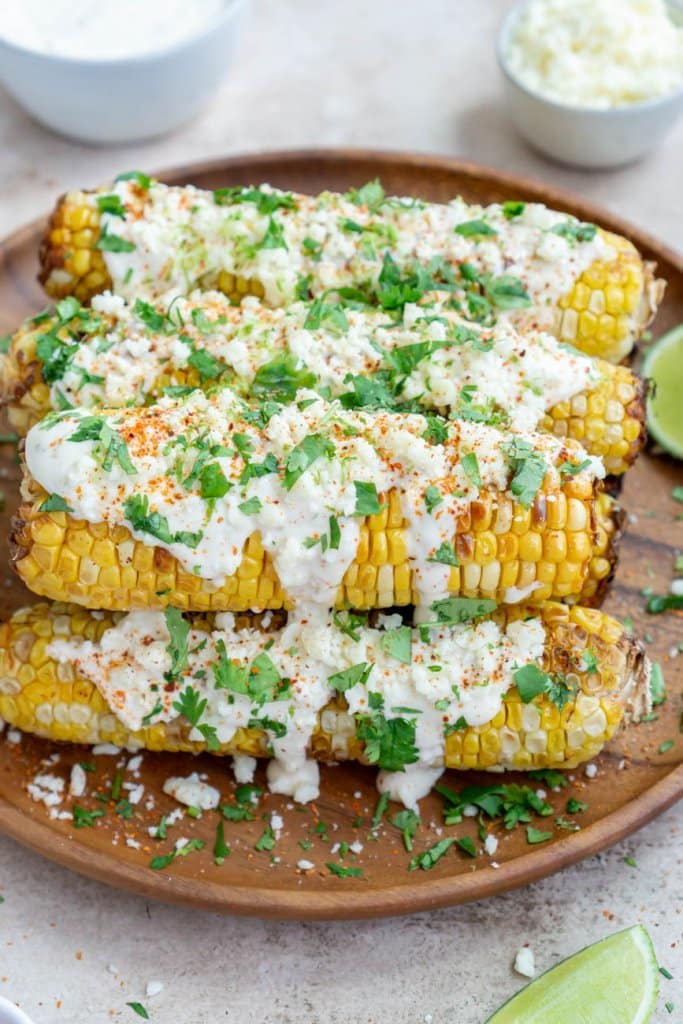 air fryer elote on a wooden plate with cotija cheese and limes on the side