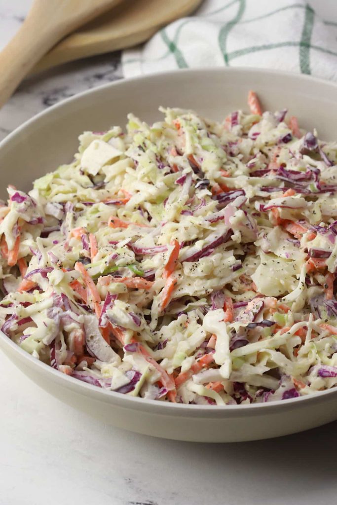 overhead view of Southern Coleslaw in white serving bowl with wooden serving spoon in background