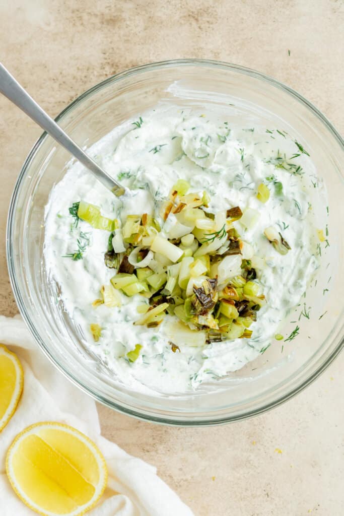 mixing whipped cottage cheese with charred scallions and herbs in a glass mixing bowl.