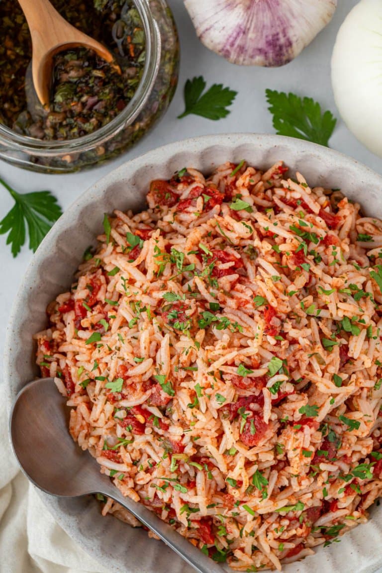 chimichurri rice in a bowl with a spoon and chimichurri sauce on the side