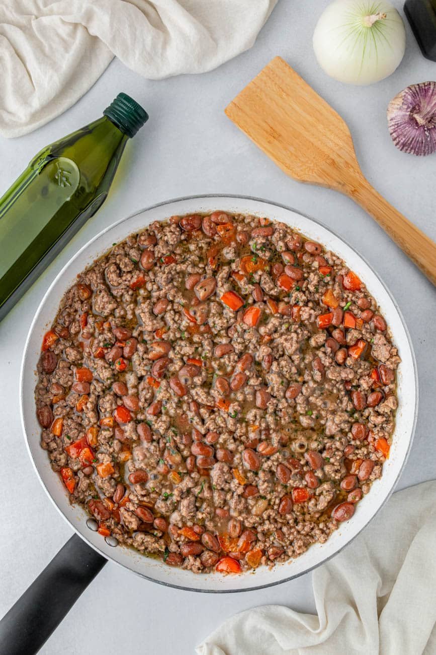 Beef empanada filling in a pan next to oil and a wooden spatula.