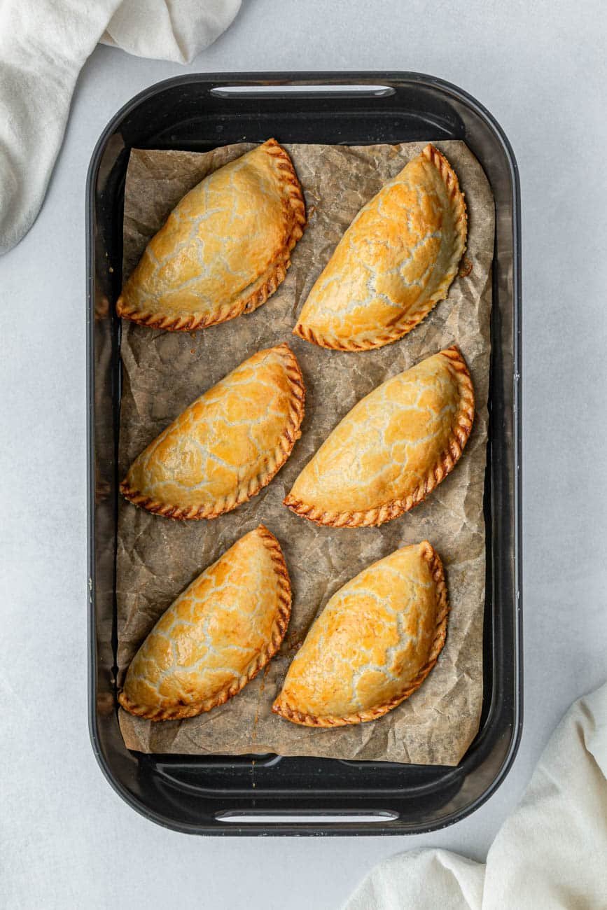 Cooked empanadas in a single layer in an air fryer basket.