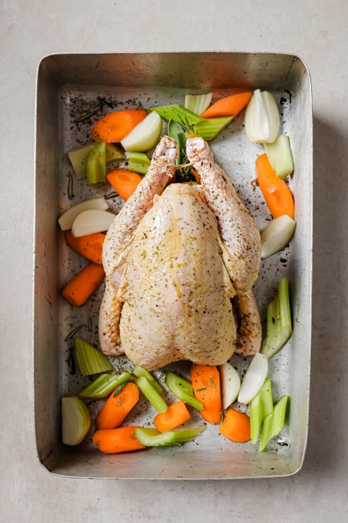 Whole chicken prepped in a roasting pan over vegetables.