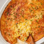baked corn casserole in a white dish with a wooden spoon