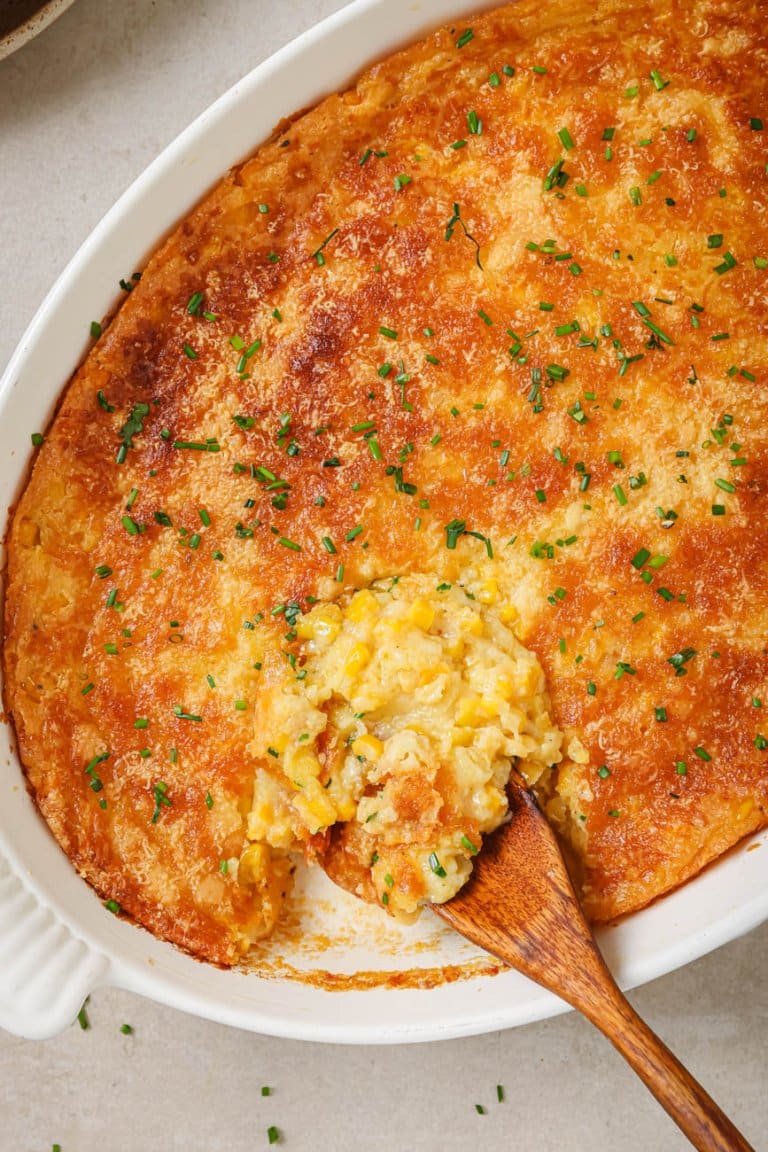 baked corn casserole in a white dish with a wooden spoon