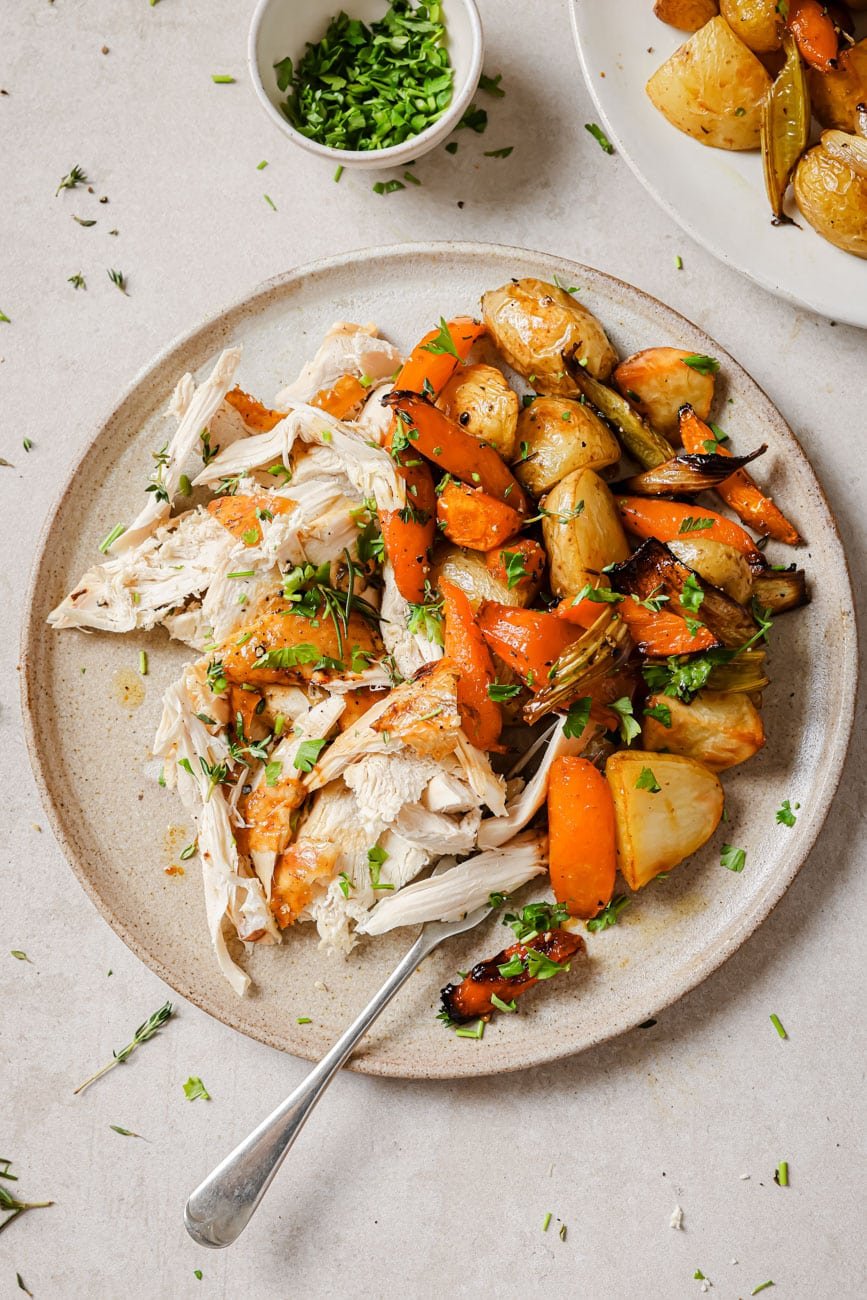 Chicken shredded on a plate with roasted vegetables.