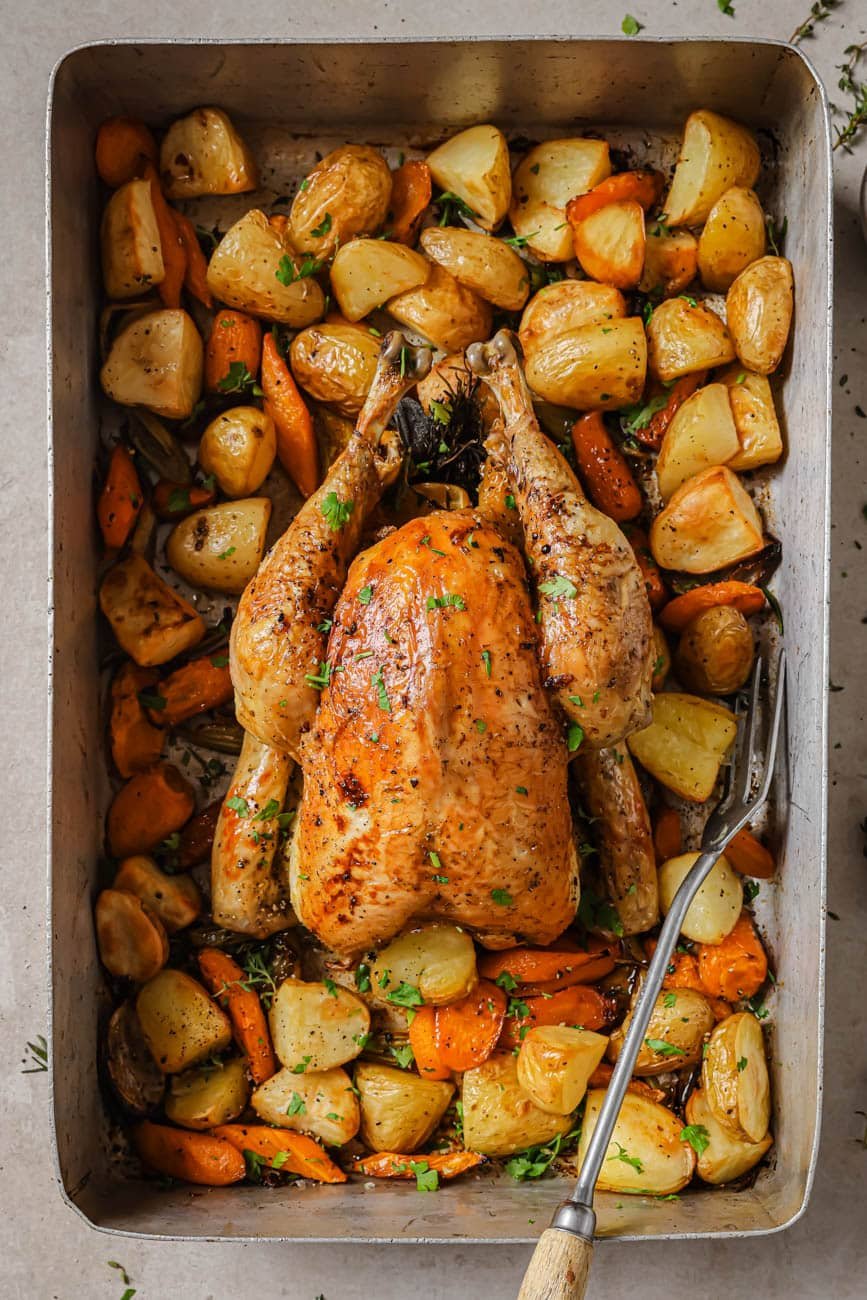 A slow roasted chicken in a roasting pan with vegetables.