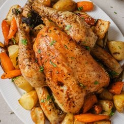 slow roasted chicken on a white serving platter with carrots and potatoes
