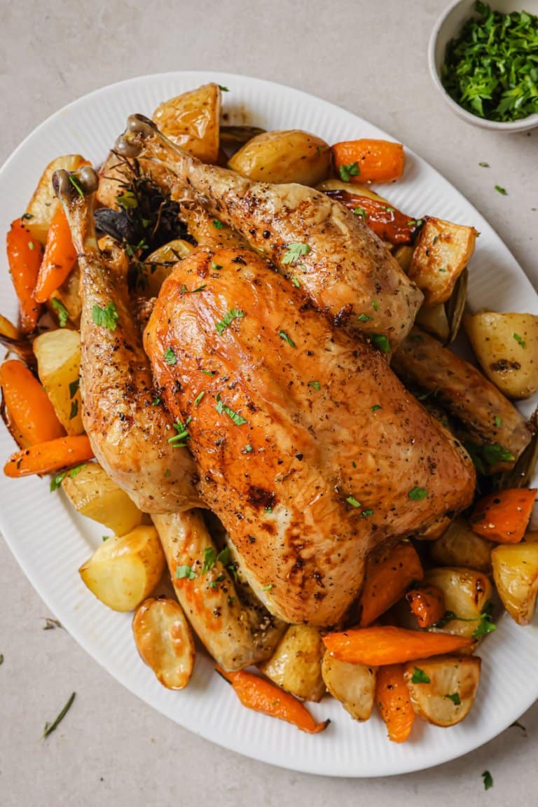 slow roasted chicken on a white serving platter with carrots and potatoes