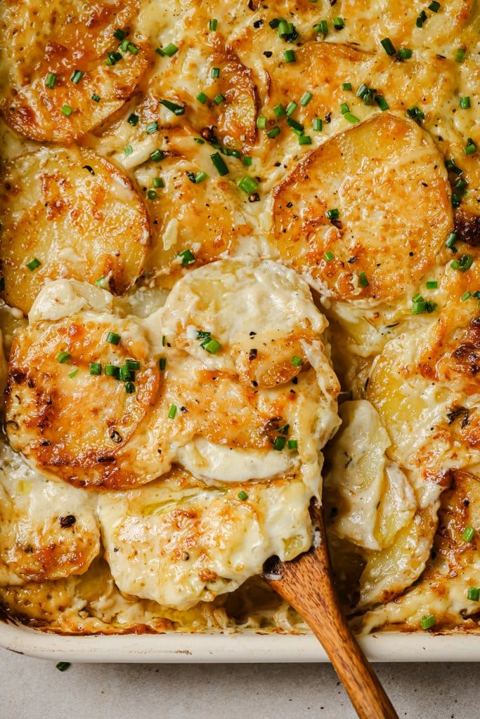 sheet pan scalloped potatoes with a wooden serving spoon