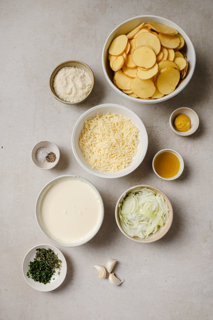 sliced potatoes, cheese, onion, cream, and spices in small ingredient bowls