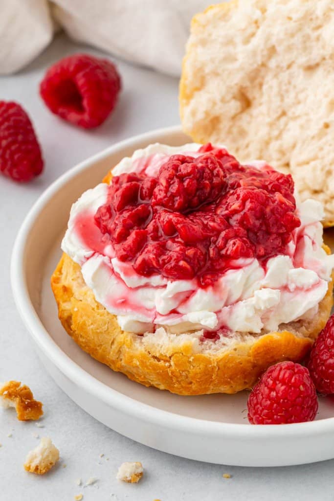 air fryer biscuit on a white plate with cream cheese and raspberries on top