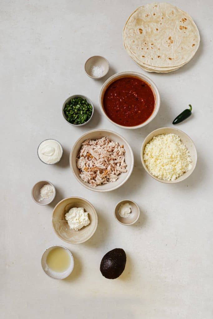 turkey, tortillas, enchilada sauce, cheese, chives, sour cream, and spices in small ingredient bowls