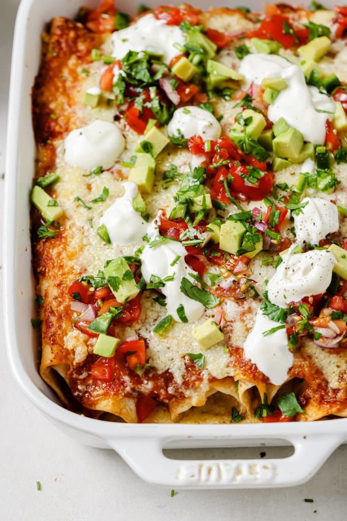 leftover turkey enchiladas in a white baking dish topped with avocado, sour cream, and tomatoes