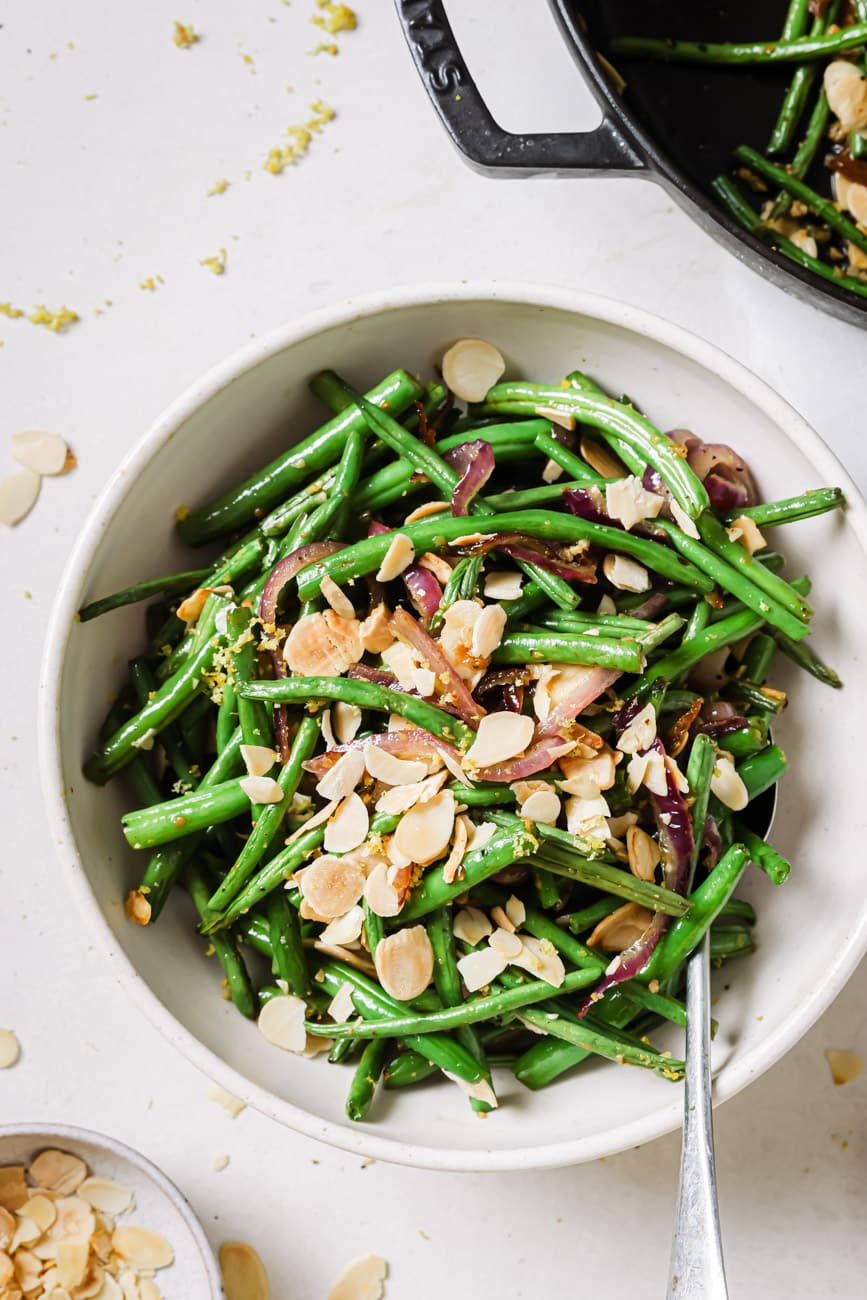 Green beans with onions and almonds in a white serving bowl with a spoon.