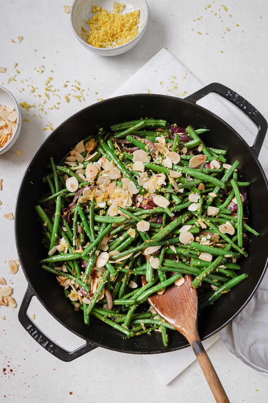 Green beans almondine in a black cast iron pan with a wooden spoon.