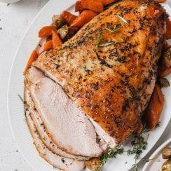 slow cooker turkey breast sliced on a white serving platter with carrots and onions