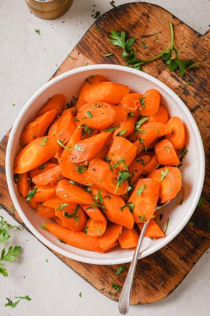 slow cooker carrots in a white bowl on a wood board with a spoon