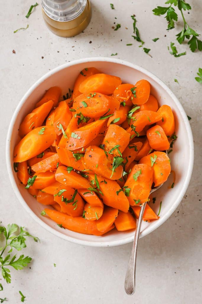 slow cooker carrots in a white bowl with herbs around
