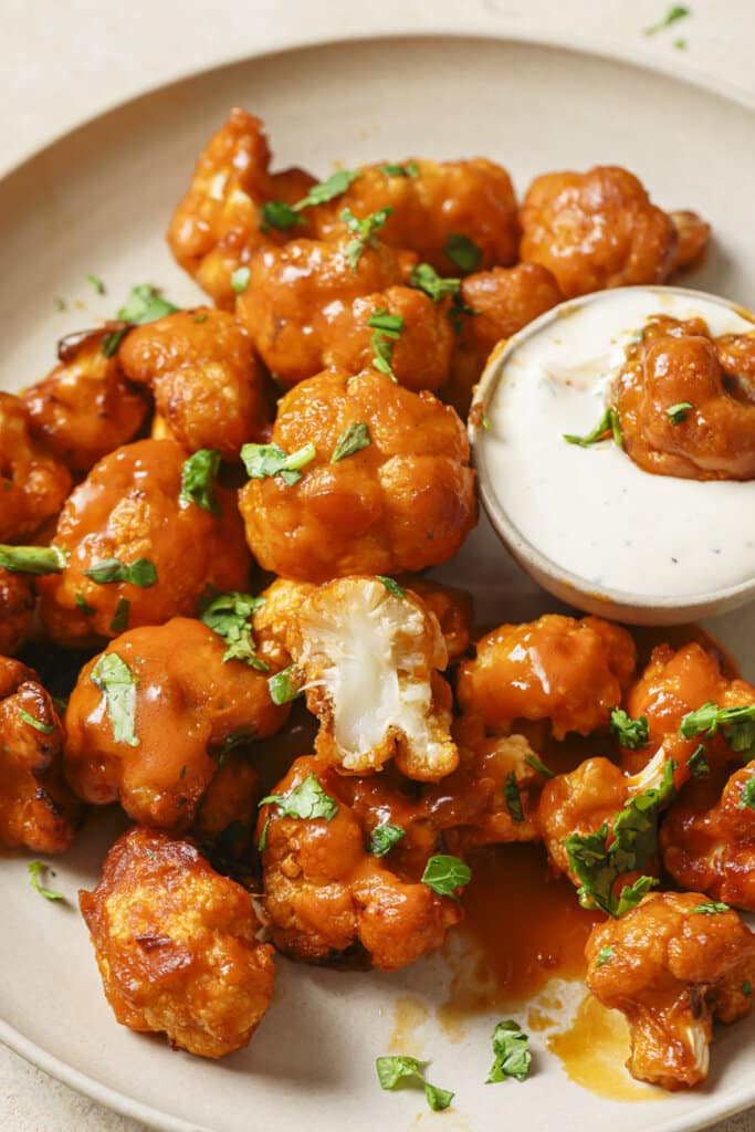 air fryer buffalo cauliflower on a plate with ranch dressing and a piece dipped in