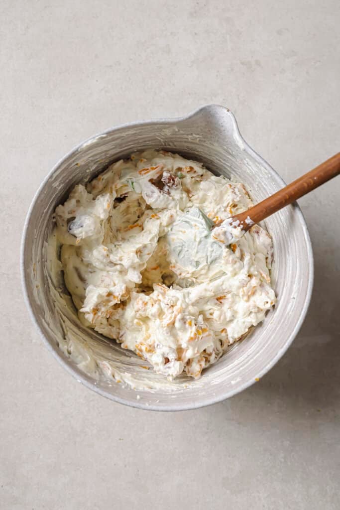 crack chicken dip ingredients mixed together in a mixing bowl with a wooden spoon.