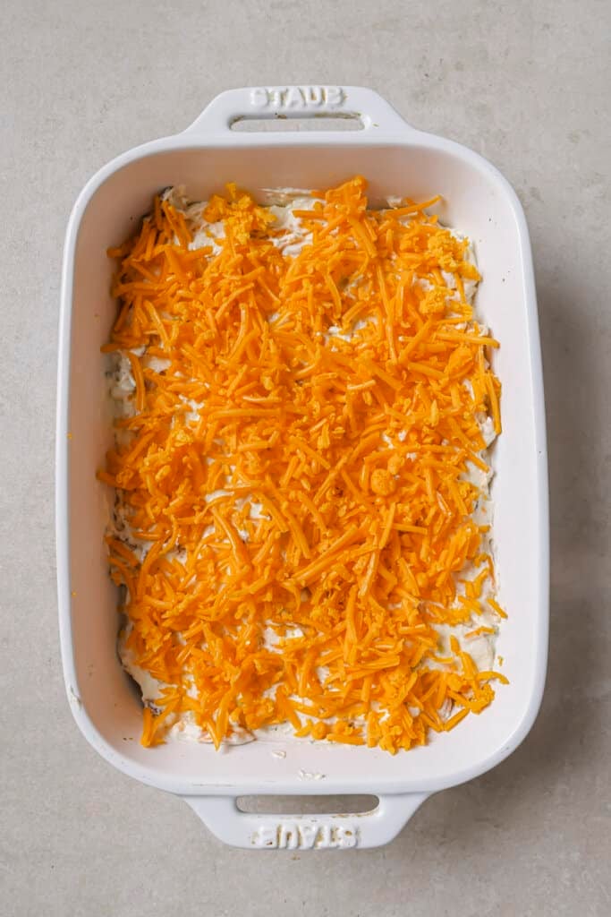 crack chicken dip in a white baking dish with shredded cheddar cheese on top before baking.