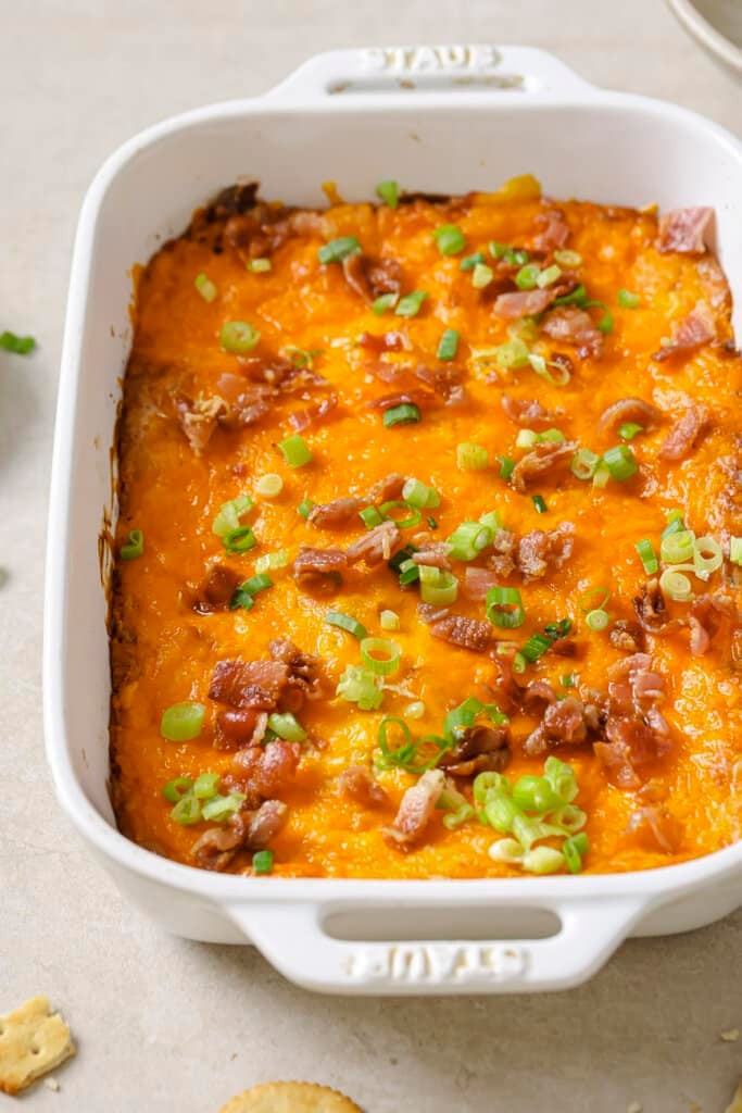 crack chicken dip in a white baking dish with bacon and green onions on top.