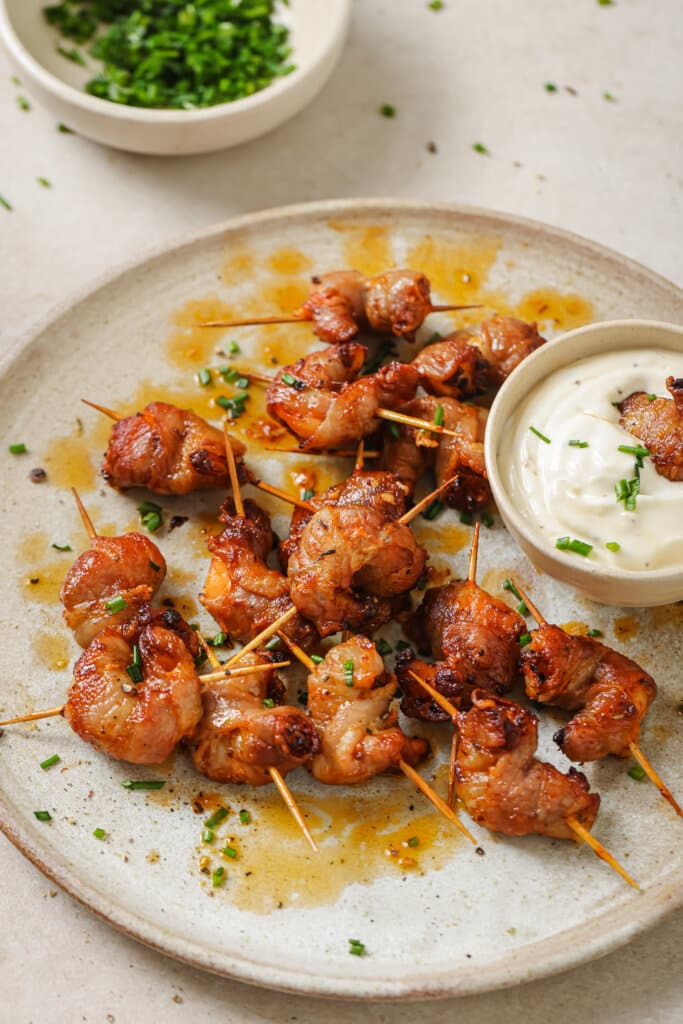 air fryer bacon wrapped shrimp on a plate, one dipped in garlic aioli