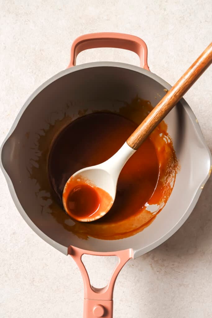 Buffalo sauce in a pan ith a silicon spoon.