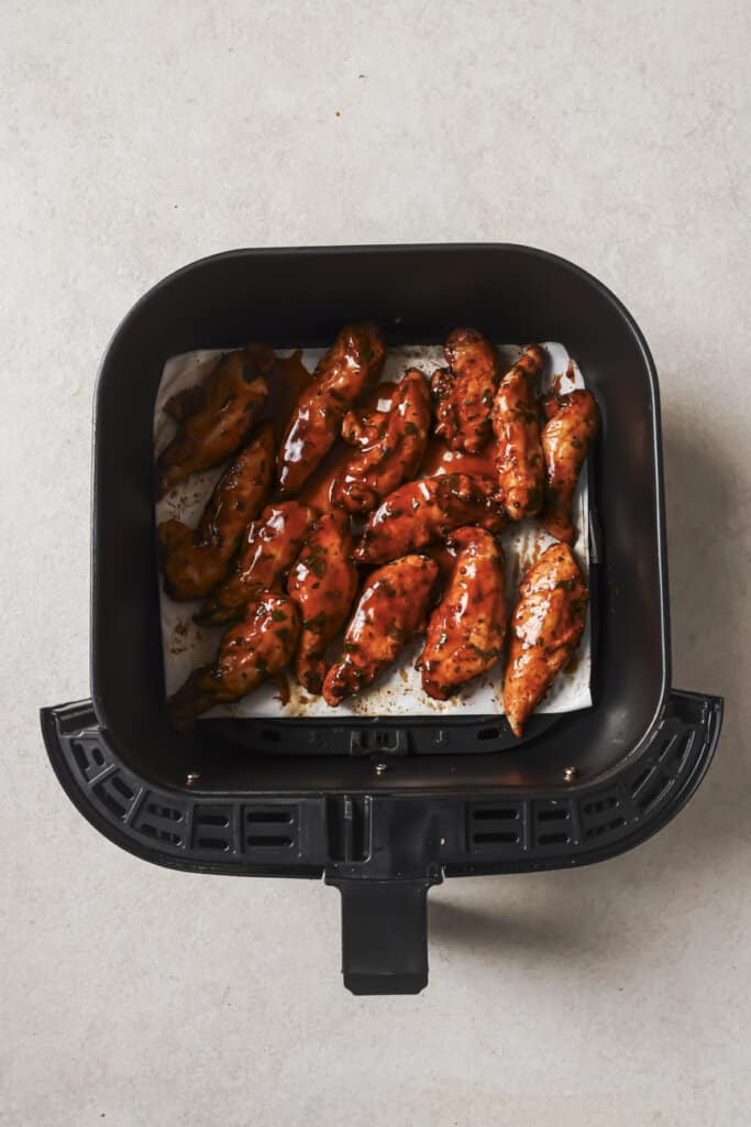 Chicken tenders coated with buffalo sauce in an air fryer.