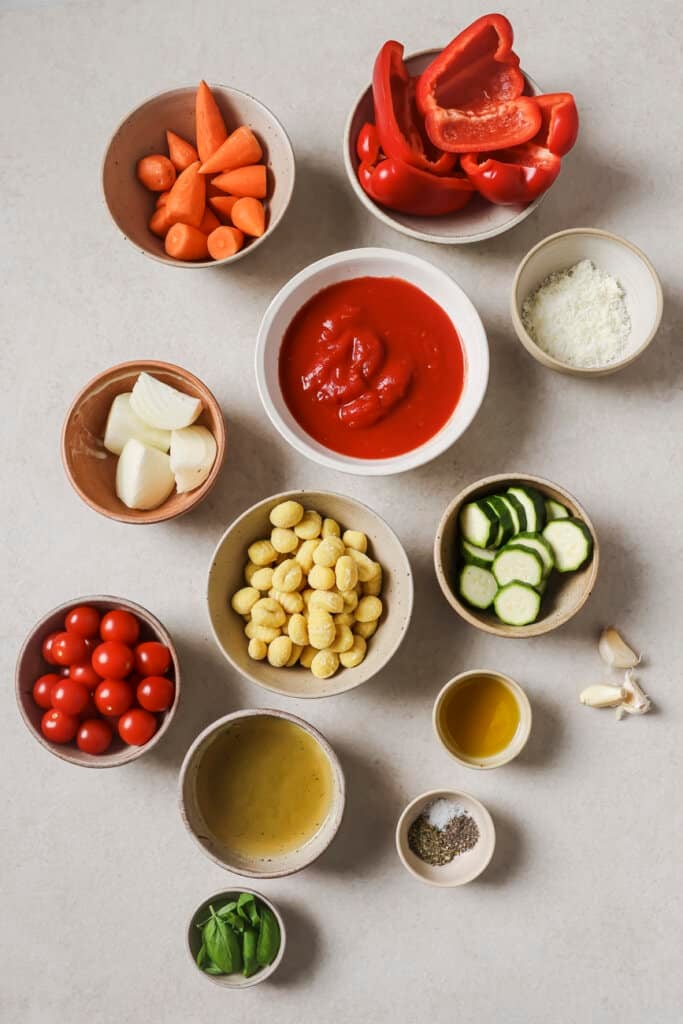 red bell peppers, tomatoes, zucchini, gnocchi, garlic, and carrots in small ingredient bowls