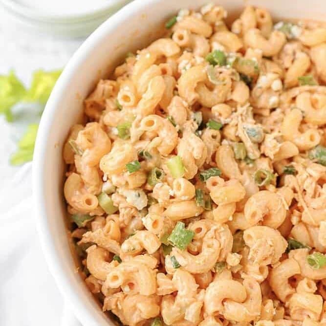 Close up of a bowl of buffalo chicken pasta salad garnished with green onions.