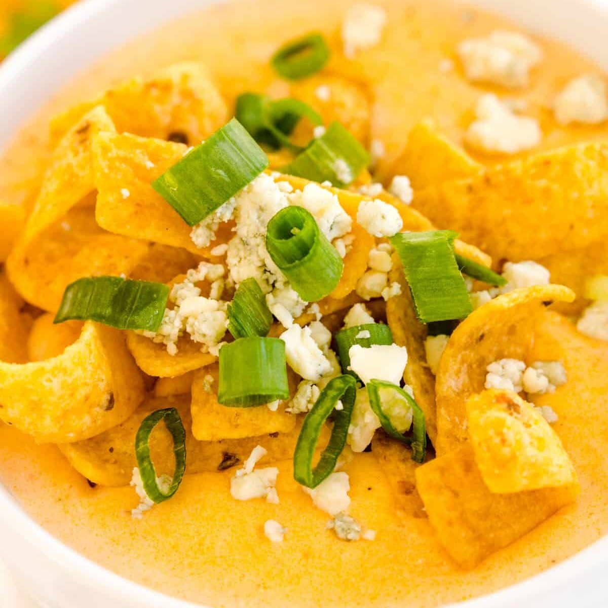 Close up image of buffalo chicken soup garnished with corn chips, green onions, and blue cheese crumbles.