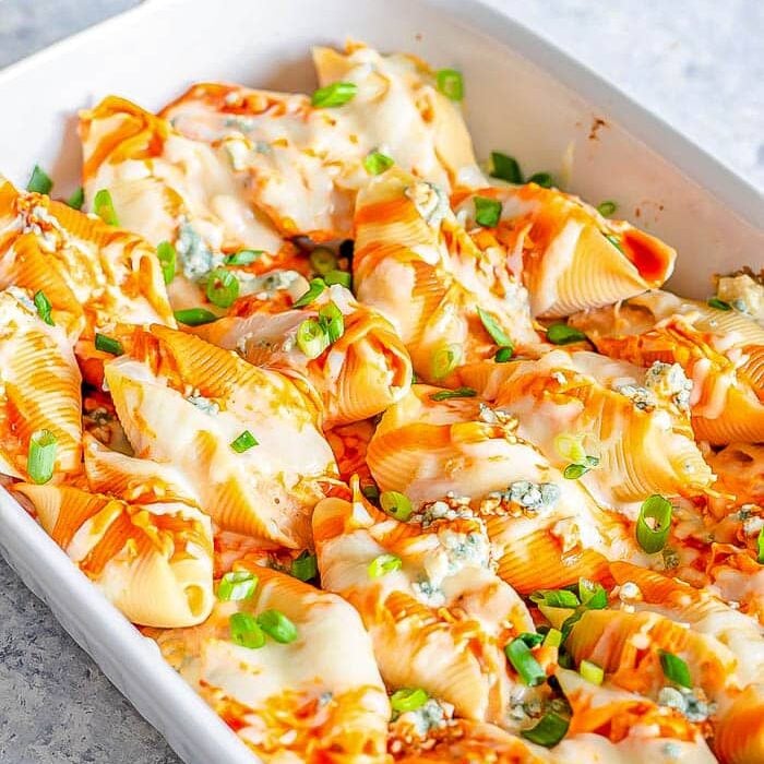 Buffalo chicken stuffed shells in a large white baking dish, drizzled with dressing and sprinkled with green onions.