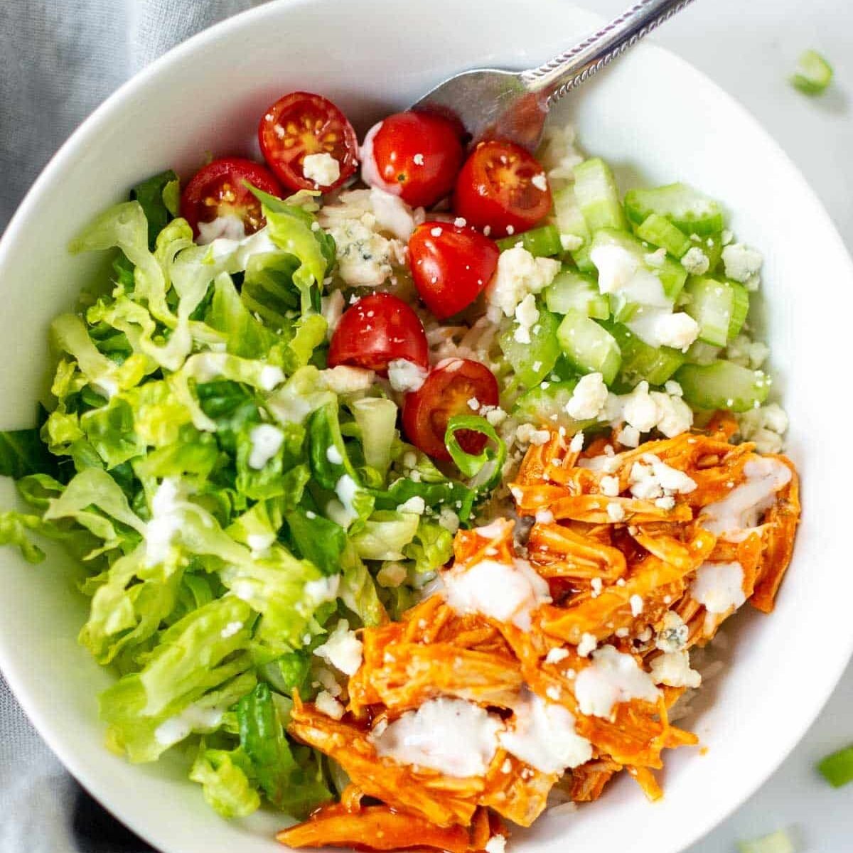 Close up of a bowl with buffalo chicken, tomatoes, lettuce, blue cheese, rice, and celery.