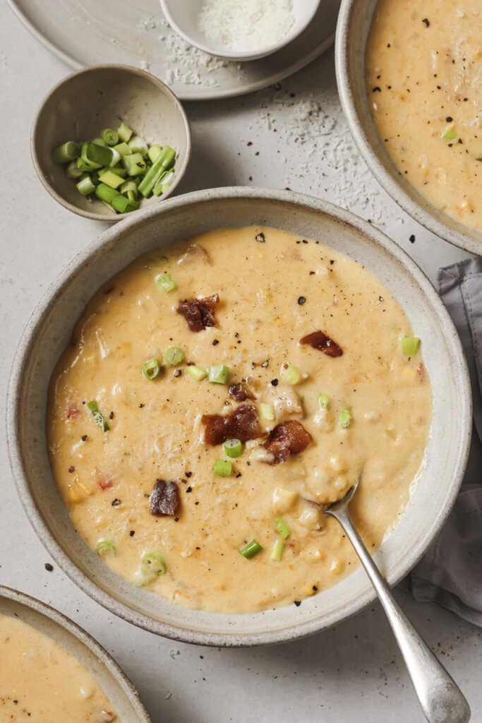 roasted corn chowder in 3 bowls, one with a spoon and topped with bacon