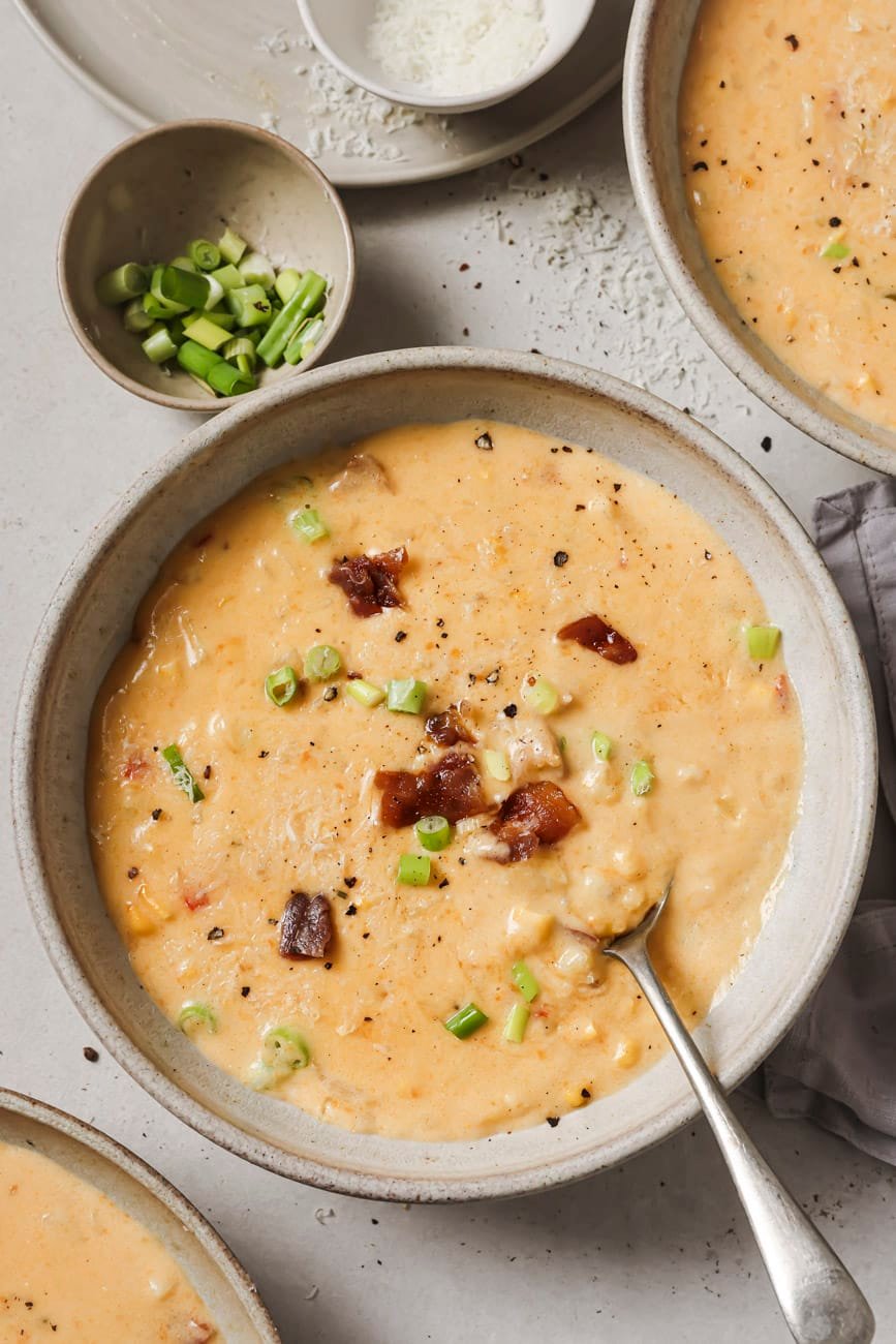 roasted corn chowder in 3 bowls, one with a spoon and topped with bacon.